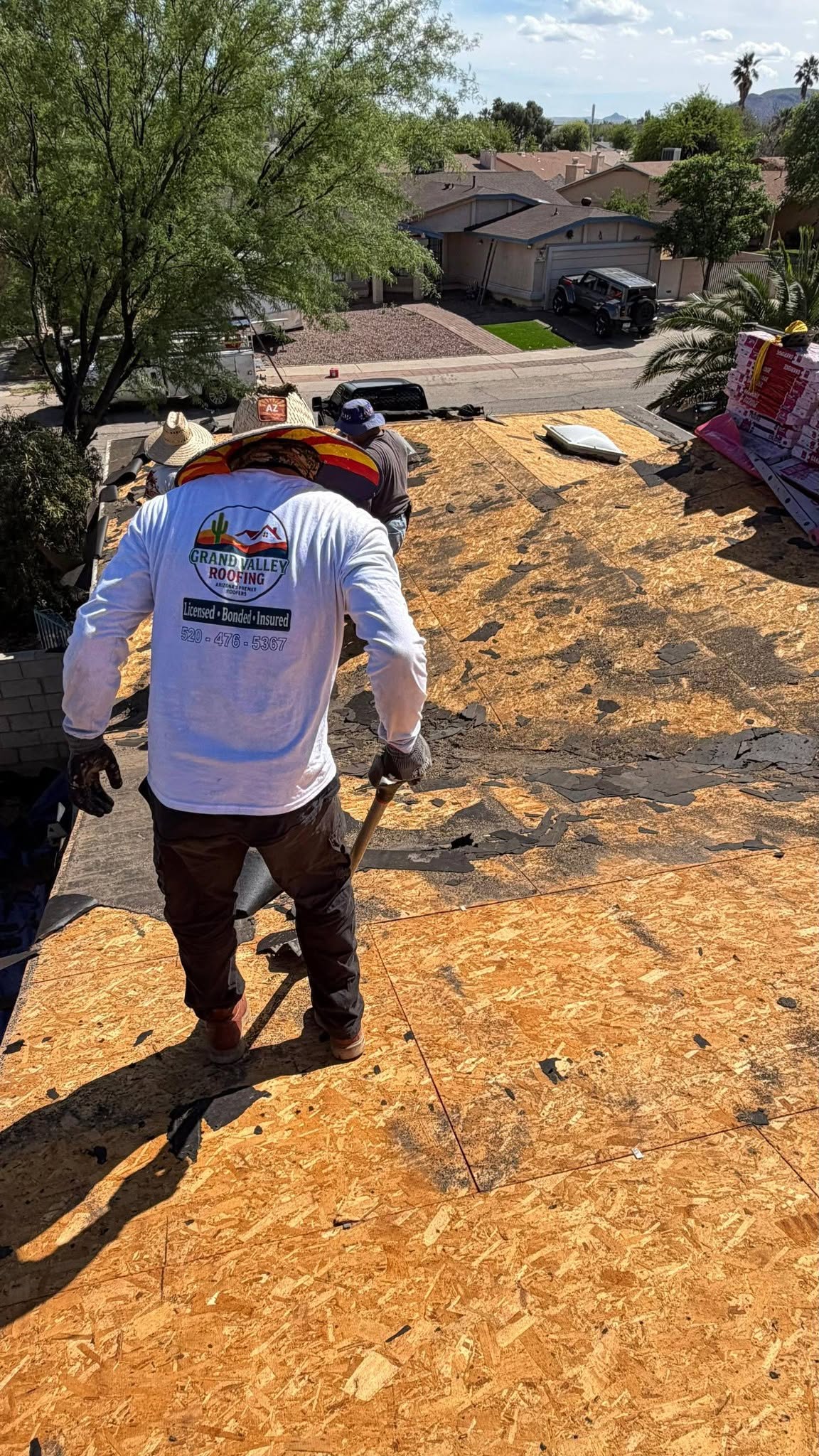 Grand Valley Roofing crew removing worn roofing material from a residential roof deck.